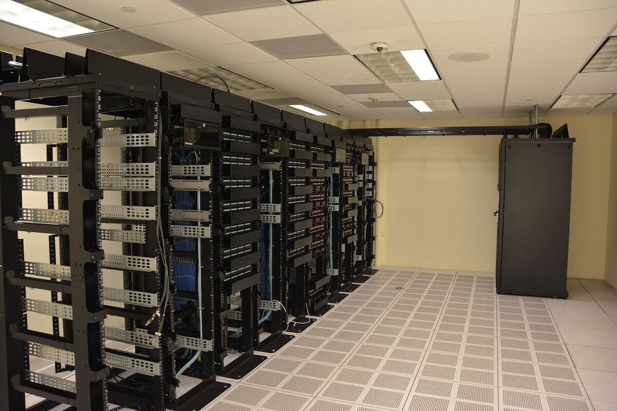 Open server racks in a data center, the hardware behind open-weight AI models like Kimi K3 and DeepSeek. Photo: Carl Lender, Wikimedia Commons, CC BY 2.0